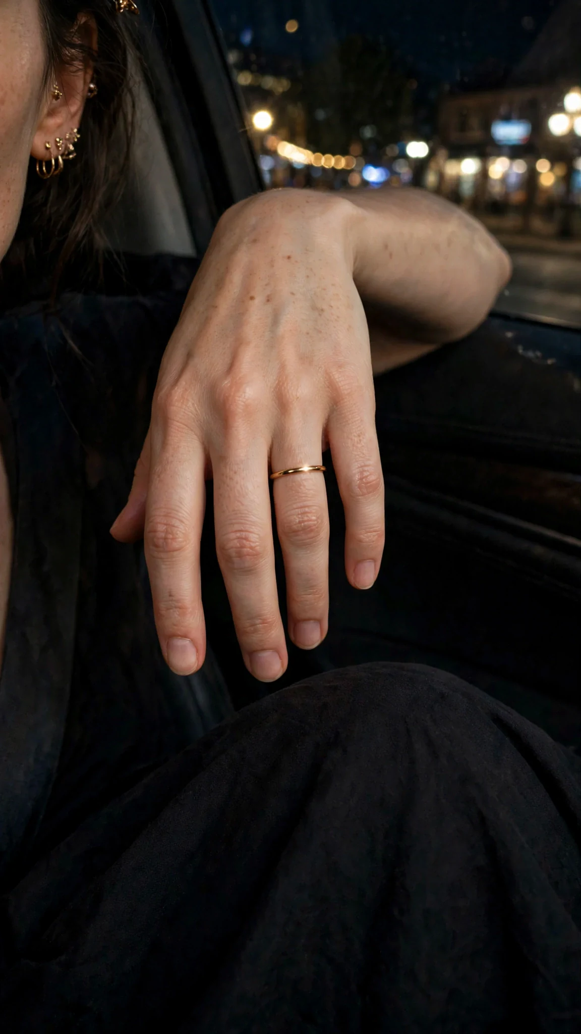Close on Rue's hand in her lap, the wedding ring catching city light.
