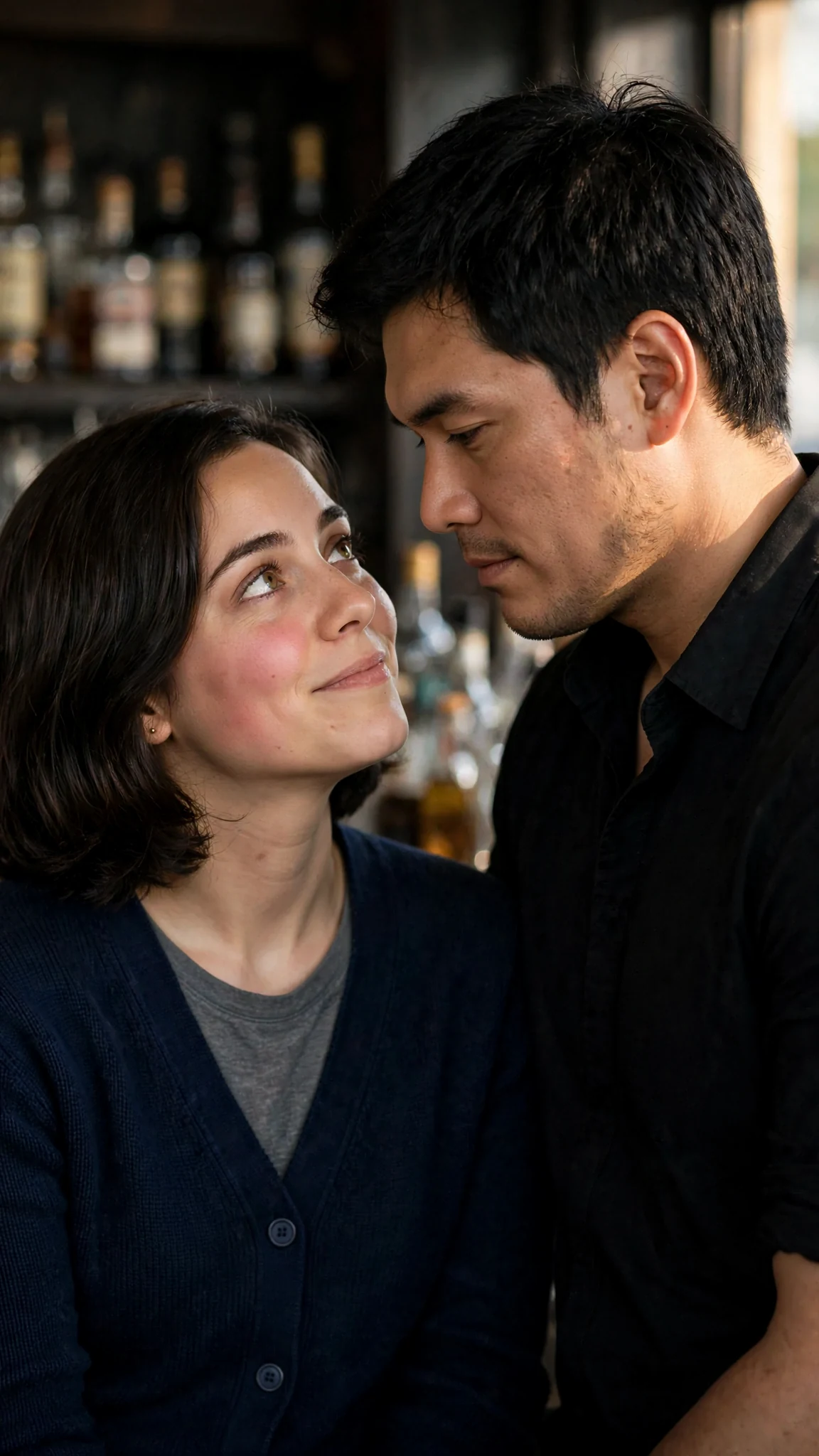 The small woman looking up at him, then dropping her eyes to the floor, both faces close and lit from the side.
