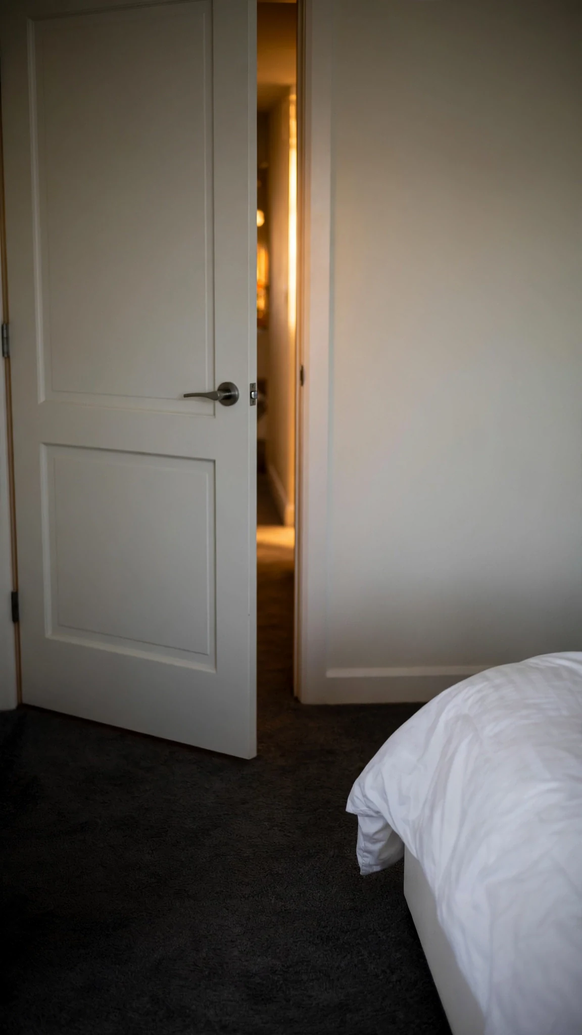 A bedroom door left open a narrow inch, warm light in the gap.