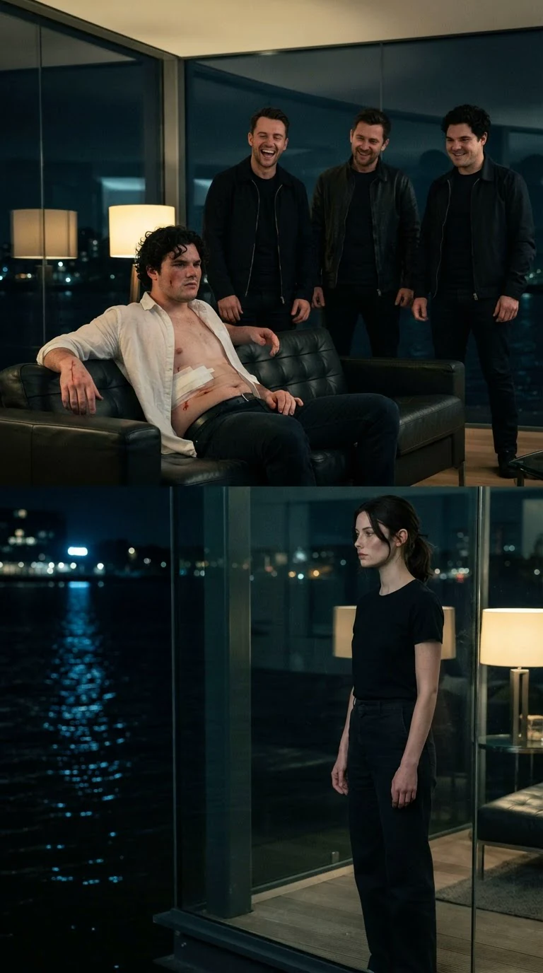 A pale injured man with curly hair sits bandaged on a couch and speaks while men in dark jackets laugh.
